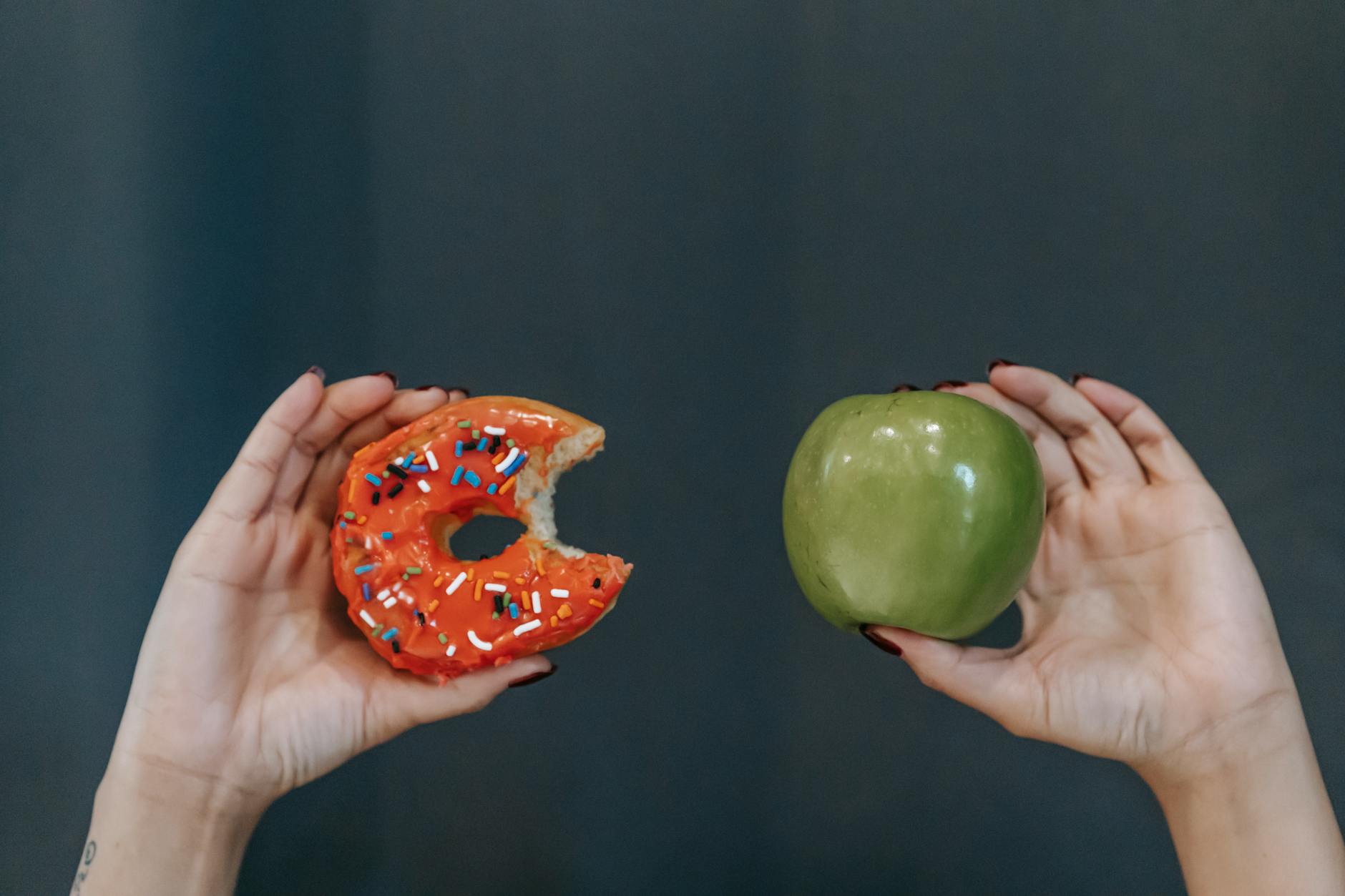 faceless woman showing fresh apple and sweet doughnut